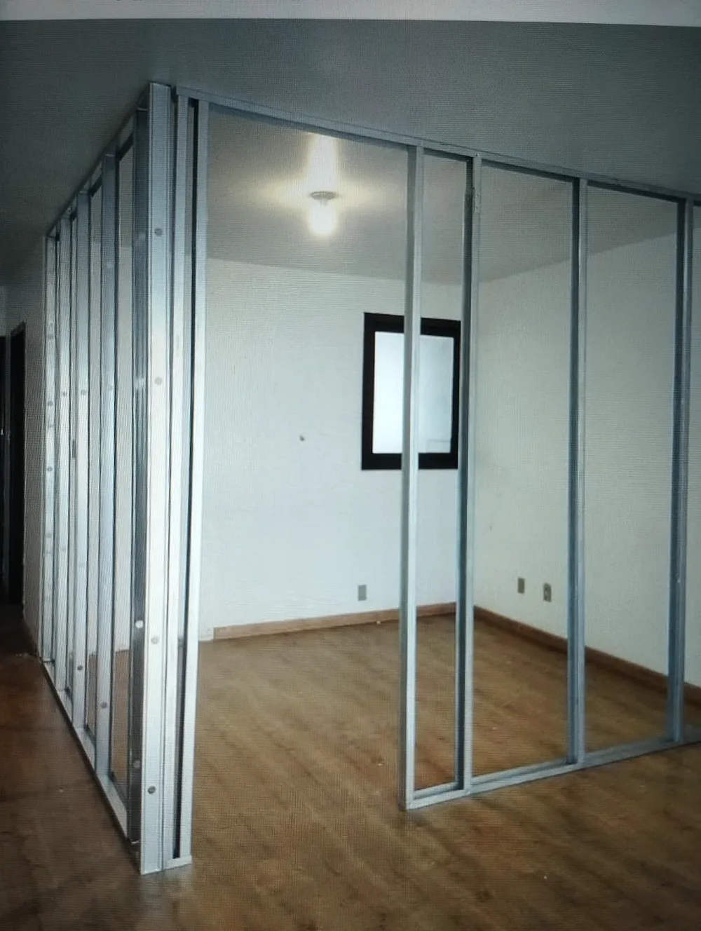 Estrutura metálica de parede de drywall montada, com guias no piso e no teto e montantes aprumados formando um ambiente.